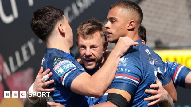 Tom Johnstone is surrounded by team-mates, all in Wakefield Trinity blue, as they celebrate one of his three tries against Bradford Bulls.