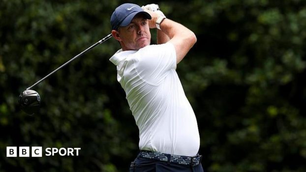 Rory McIlroy at the Truist Championship, wearing a white golf shirt and blue cap, swinging a metal wood